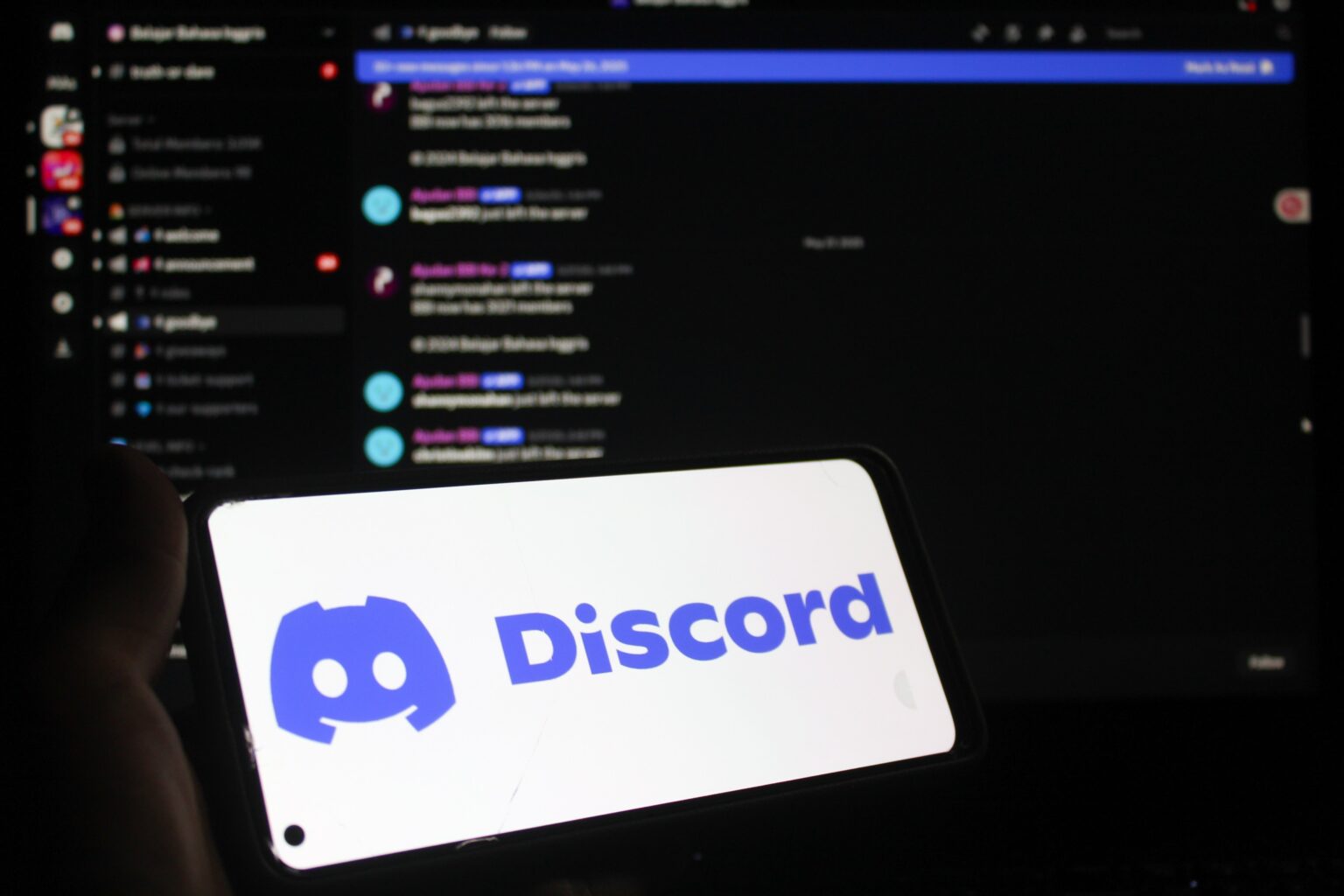 Smartphone mostrando el logotipo de Discord con la interfaz de la aplicación de fondo en una pantalla de computadora.