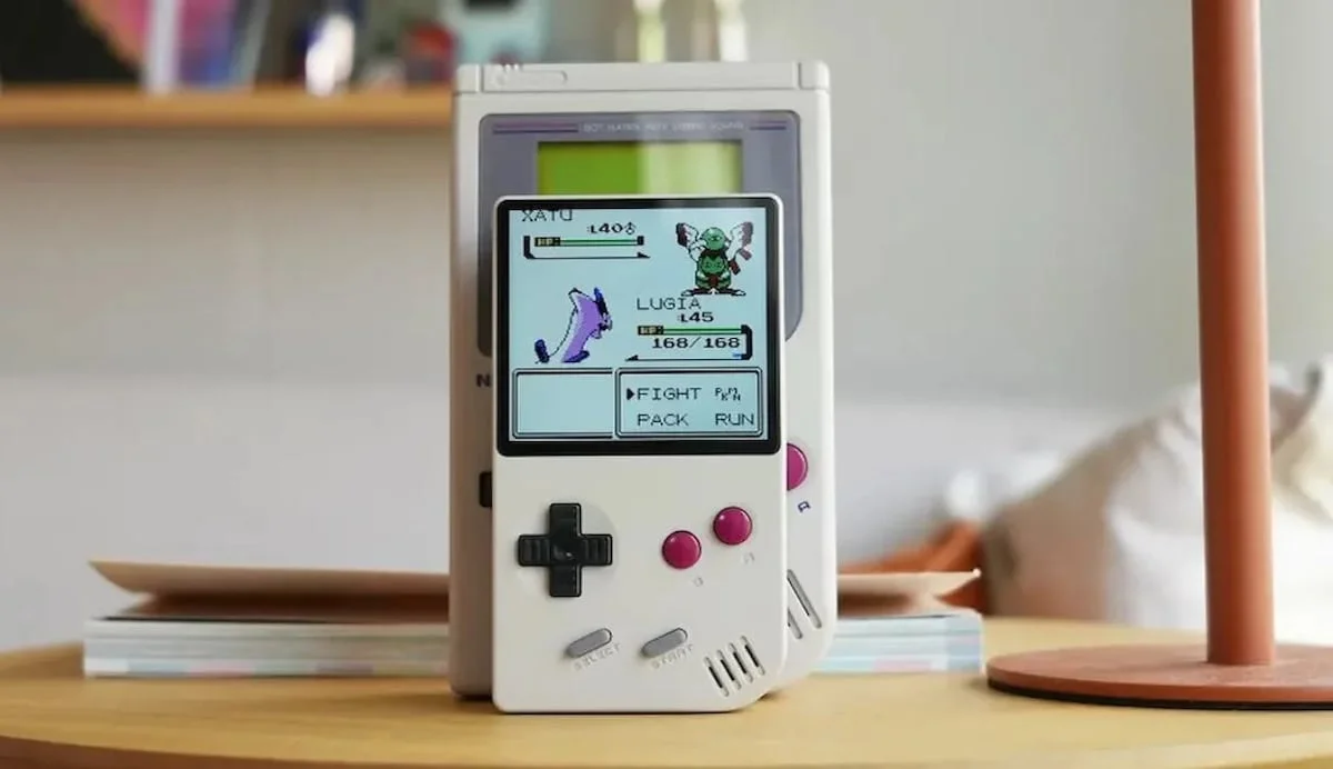 Consola portátil blanca estilo Game Boy con pantalla a color mostrando un juego clásico de Pokémon.